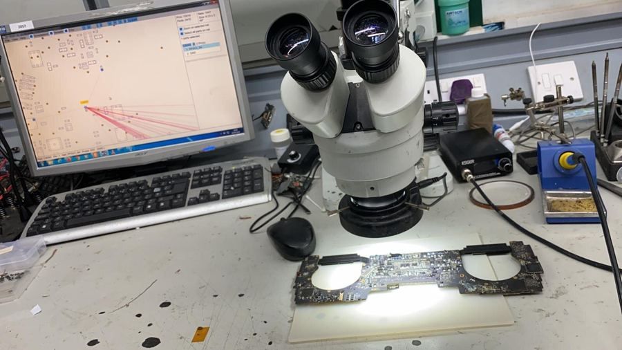 A MacBook logic board under the microscope beside the soldering station